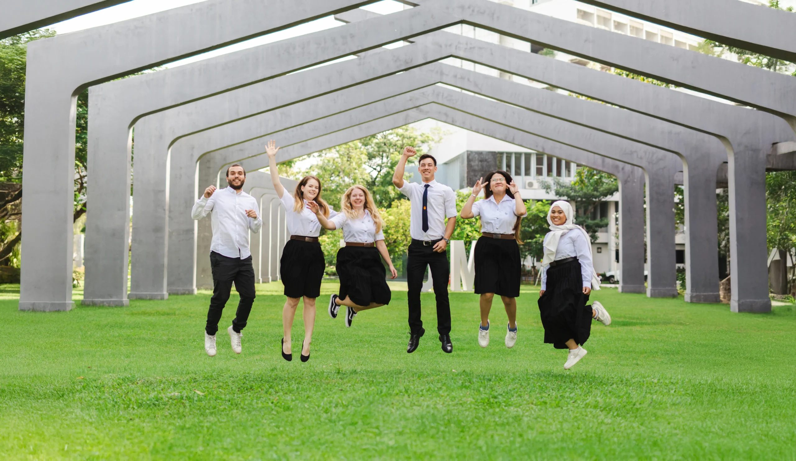 Students together on a green lawn beneath geometric campus arches at KMUTT.